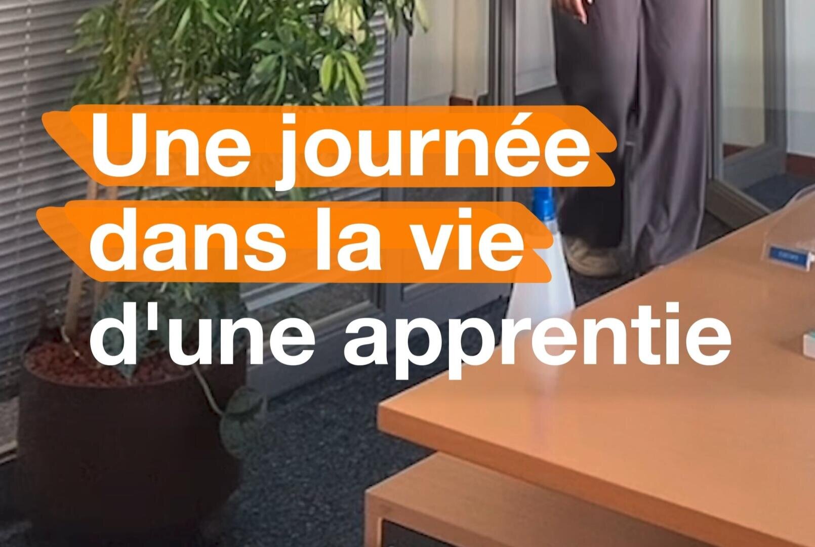Une personne se tient debout sur une chaise dans un bureau à côté d'une plante et d'un bureau. Le texte orange et blanc superposé en français se lit comme suit : "Une journée dans la vie d'une apprentie : Une journée dans la vie d'une apprentie.