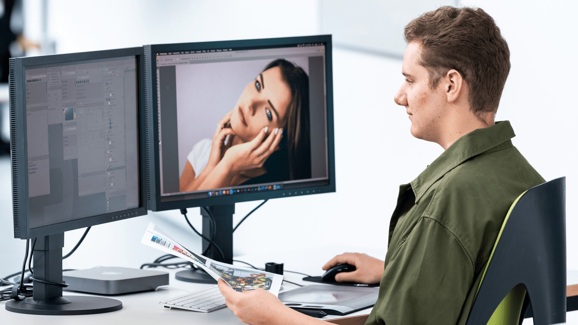 Une personne assise à un bureau travaille à la retouche de photos à l'aide de deux écrans d'ordinateur, dont l'un affiche un portrait de femme en gros plan. Elle tient un magazine et utilise une souris d'ordinateur.