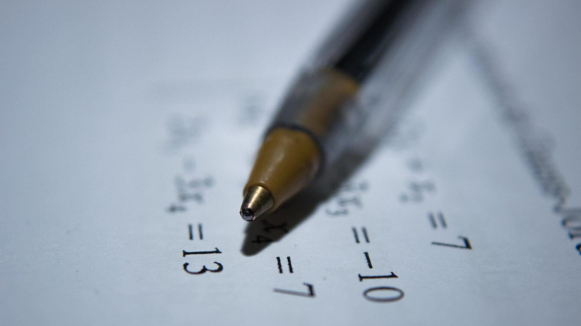 Gros plan sur un stylo à bille posé sur une feuille de papier contenant des équations mathématiques, dont l'une des solutions est "= 13". L'accent est mis sur la pointe du stylo et sur les problèmes mathématiques.