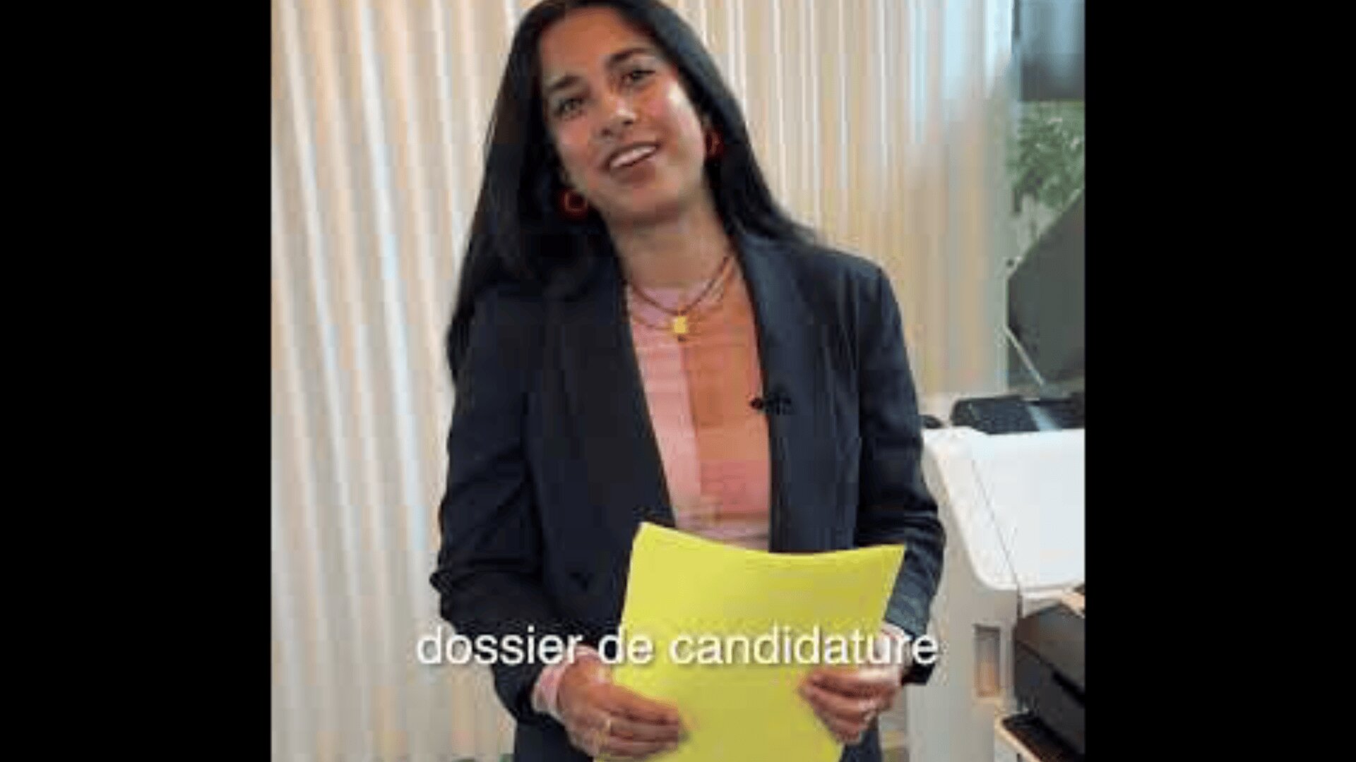 Une femme aux longs cheveux noirs tient des papiers jaunes et se tient devant une fenêtre aux stores blancs. Elle est souriante et porte un blazer. Le texte français "dossier de candidature" apparaît sur l'image.