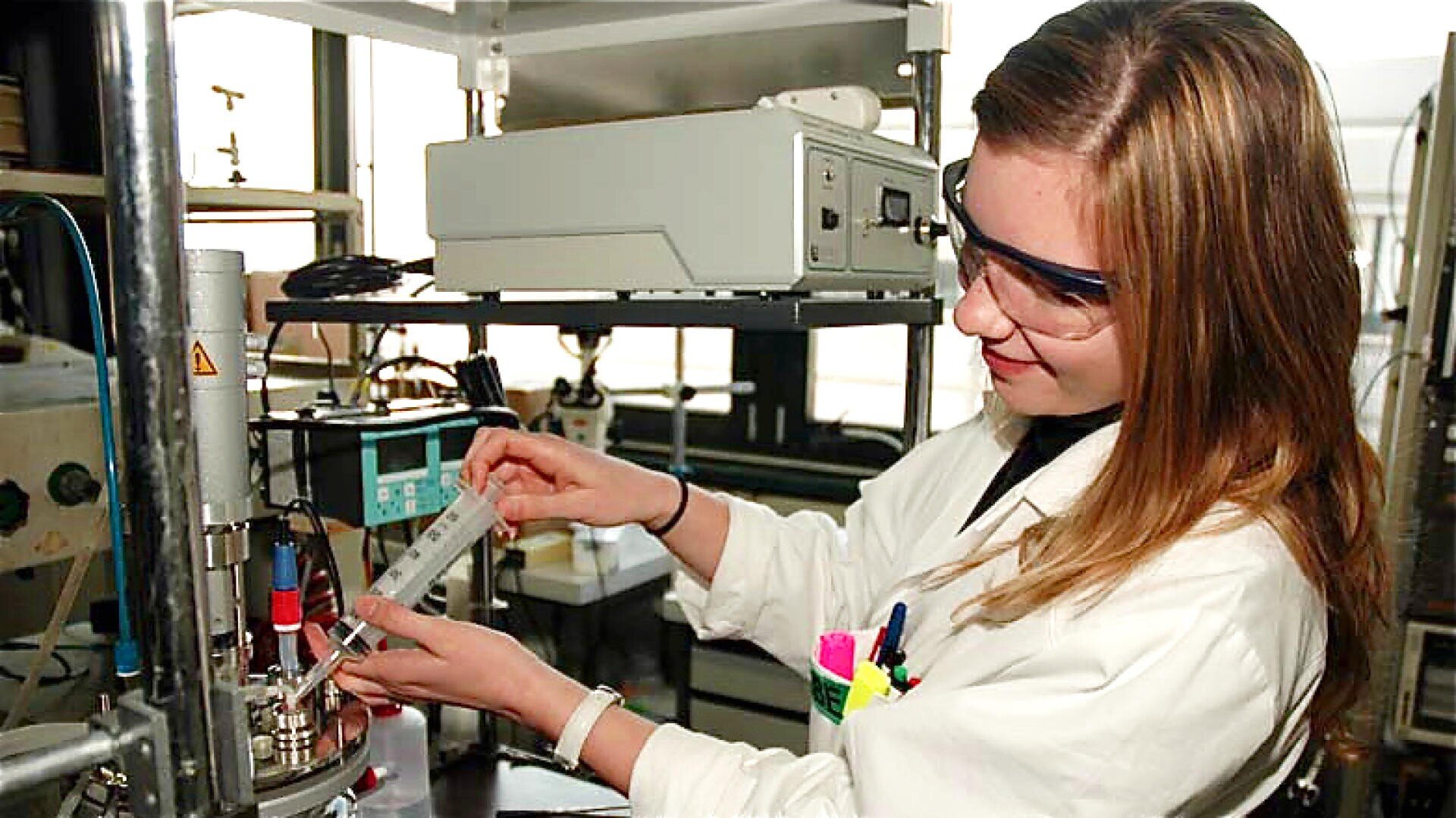 Une femme portant des lunettes de protection et une blouse de laboratoire utilise une seringue pour injecter un liquide dans un équipement de laboratoire dans un laboratoire scientifique.