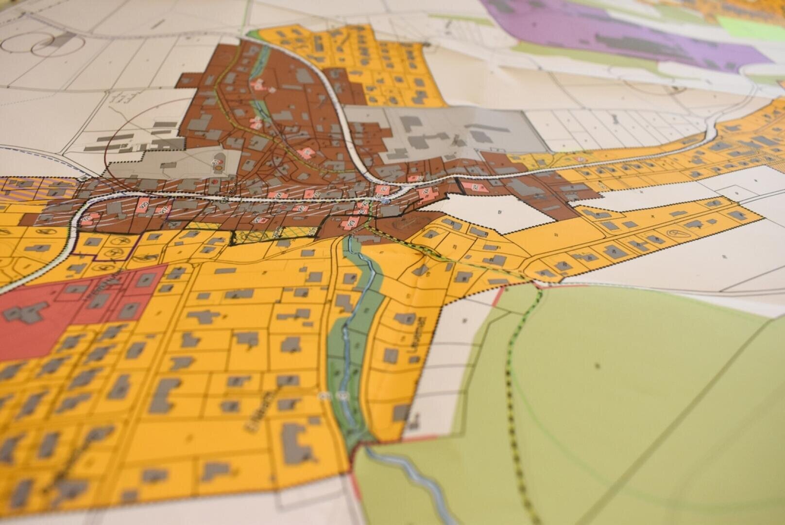 Gros plan sur une carte d'urbanisme colorée montrant différentes zones en jaune, marron, gris et vert, avec des rues, des terrains et une rivière traversant la zone centrale.