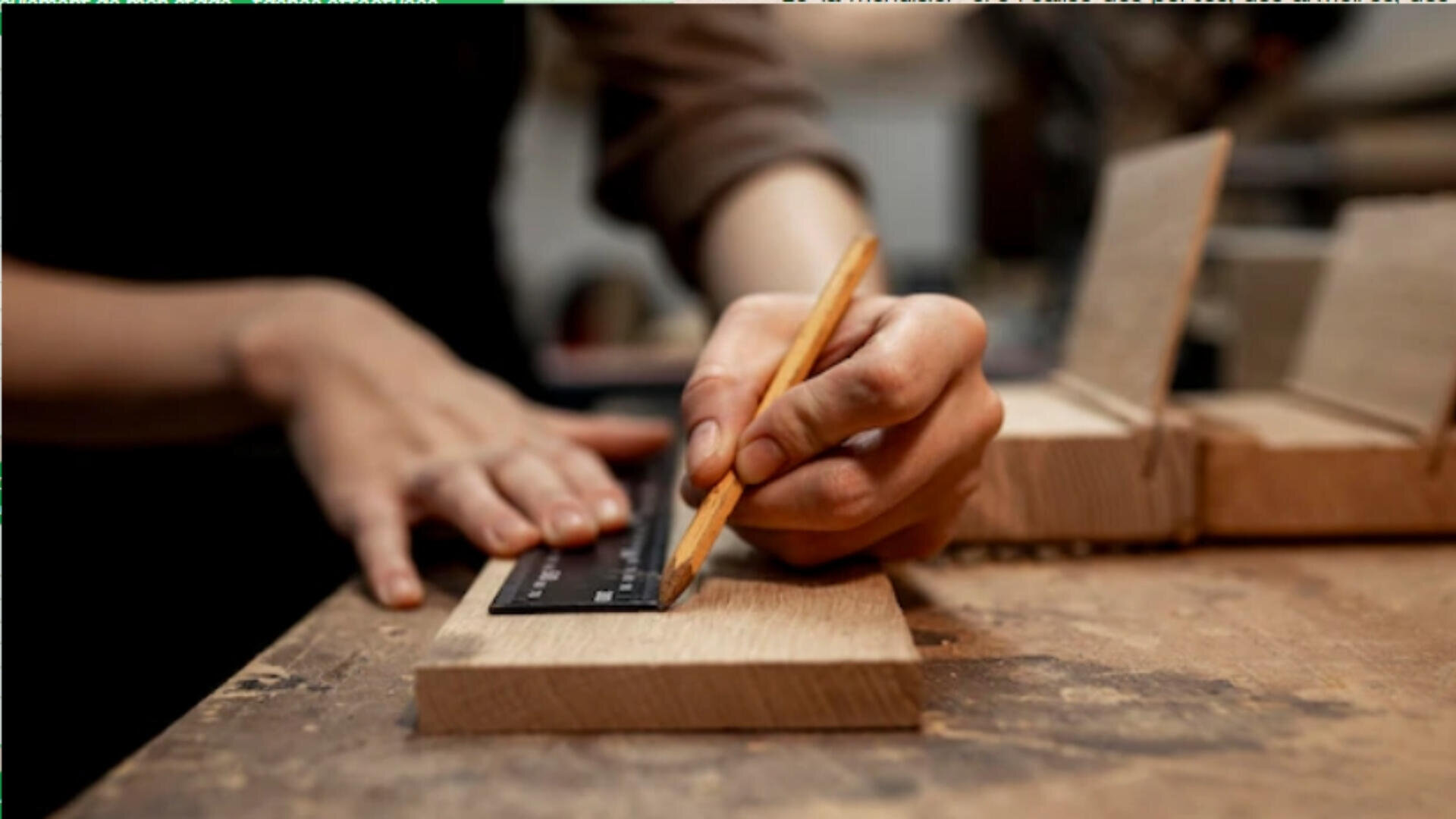 Une personne utilise un crayon et une règle pour marquer des mesures sur un morceau de bois, se préparant ainsi au travail du bois dans un atelier.
