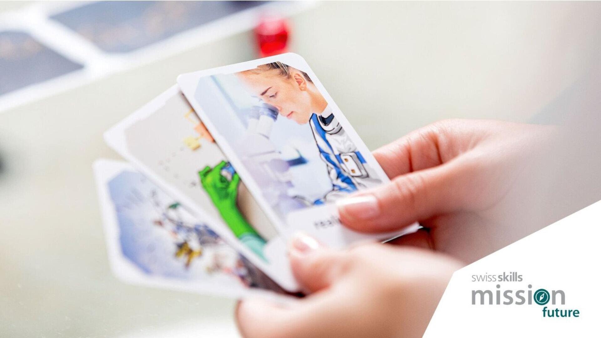 Une personne tient trois cartes, dont l'une représente un scientifique utilisant un microscope. Le logo SwissSkills Mission Future apparaît dans le coin inférieur droit.